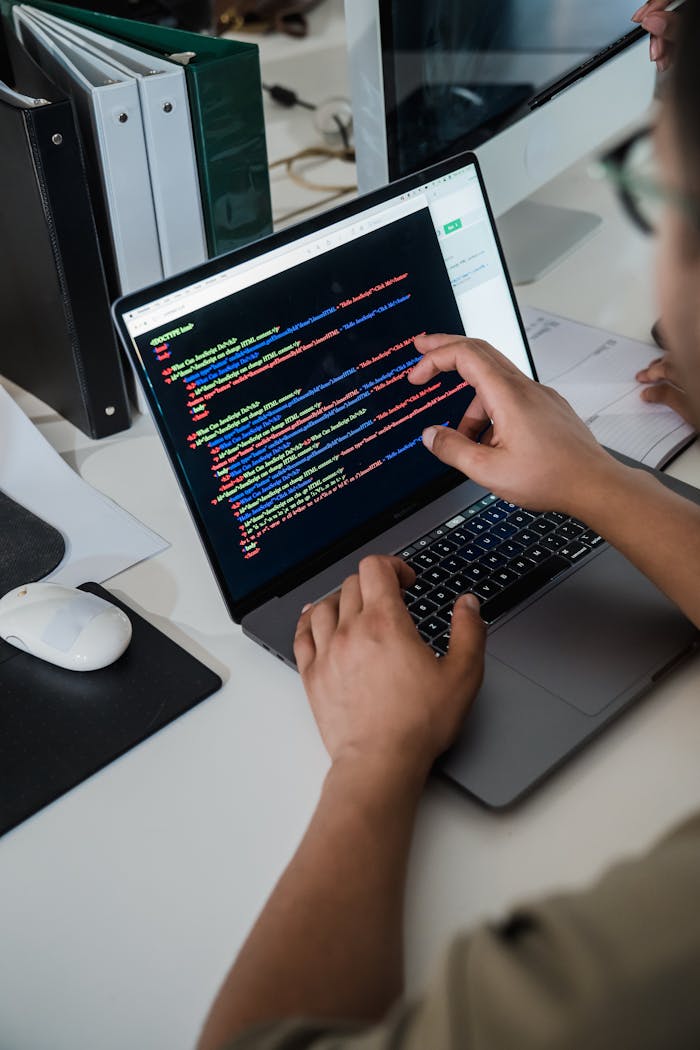 services-01 Close-up of a programmer pointing at a colorful code script on a laptop in an office setting.